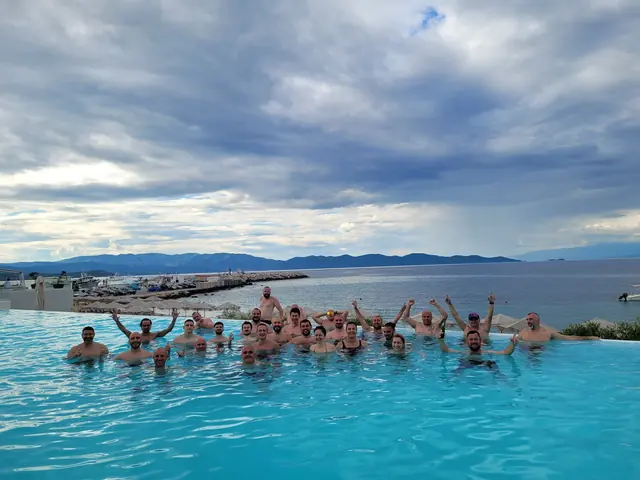 The team in an infinity pool overlooking the sea, arms raised